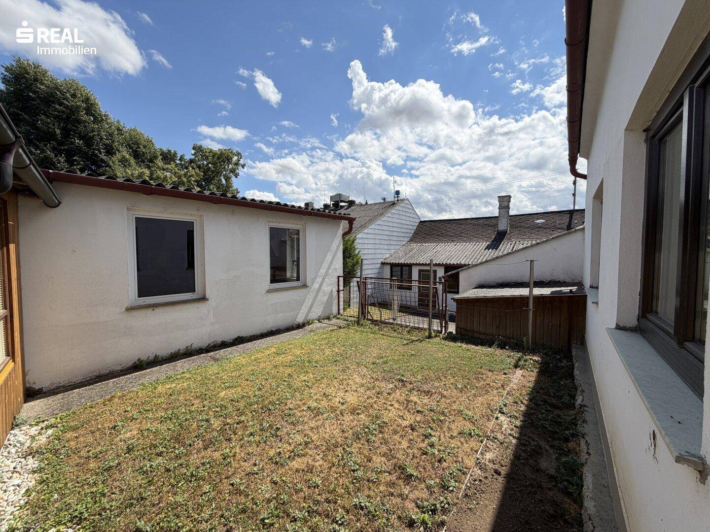 Kleiner Gartenbereich hinter dem Haus mit Rasenfläche und Blick auf angrenzende Gebäude.