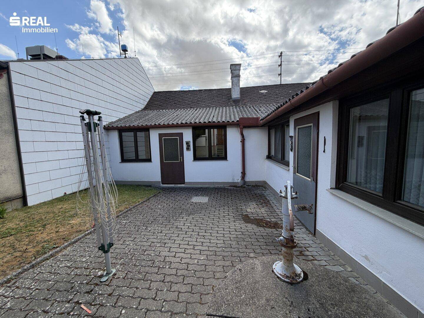 Gepflasterter Hofbereich hinter dem Haus mit Wäscheständer und Nebengebäuden.