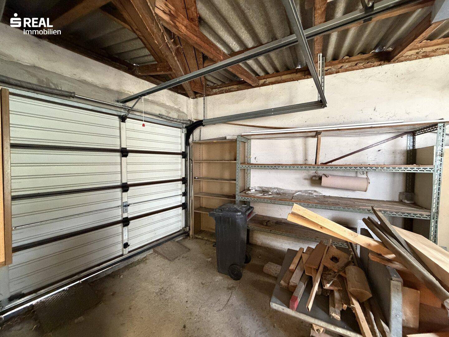 Innenansicht einer Garage mit Rolltor, Regalen und Holzkonstruktion der Decke.