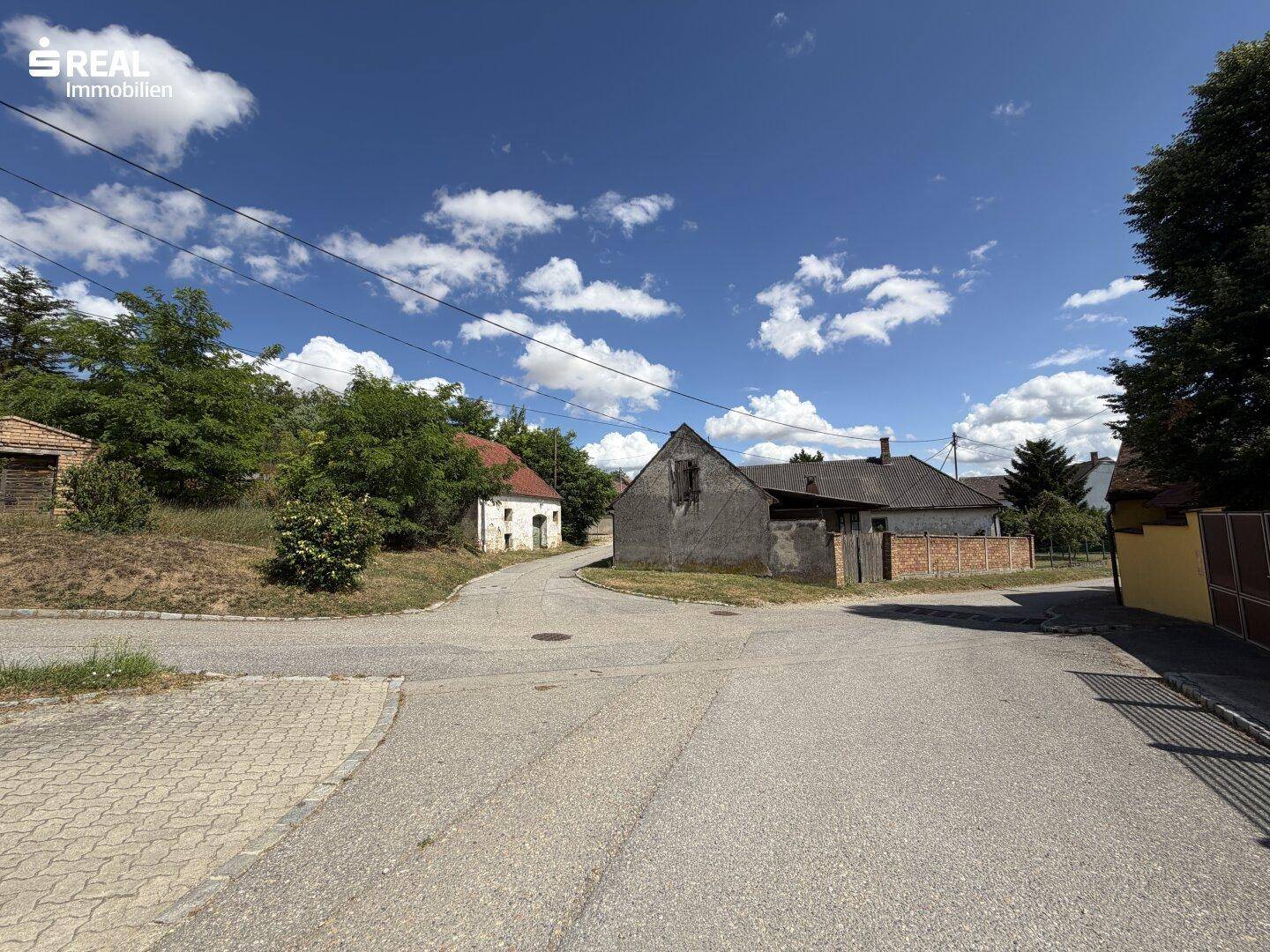 Ländliche Umgebung mit Straßenkreuzung und älteren Gebäuden unter blauem Himmel.