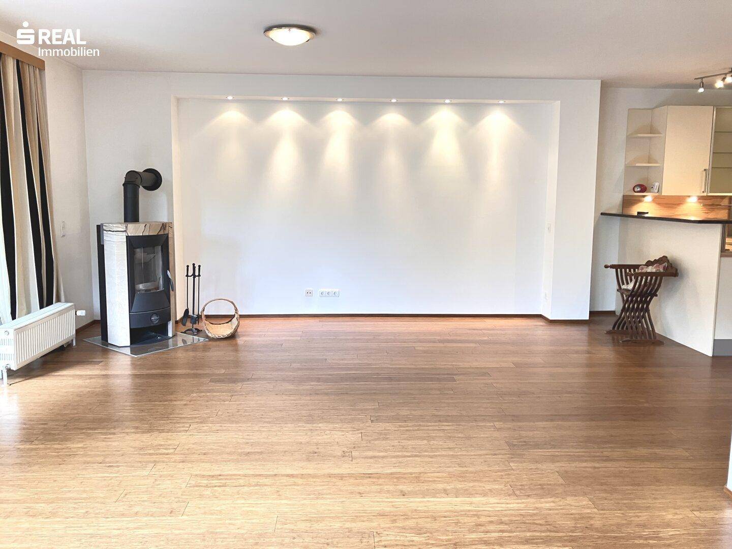 Offener Wohnbereich mit Holzboden, Kaminofen und einer Wand mit integrierten Deckenstrahlern.