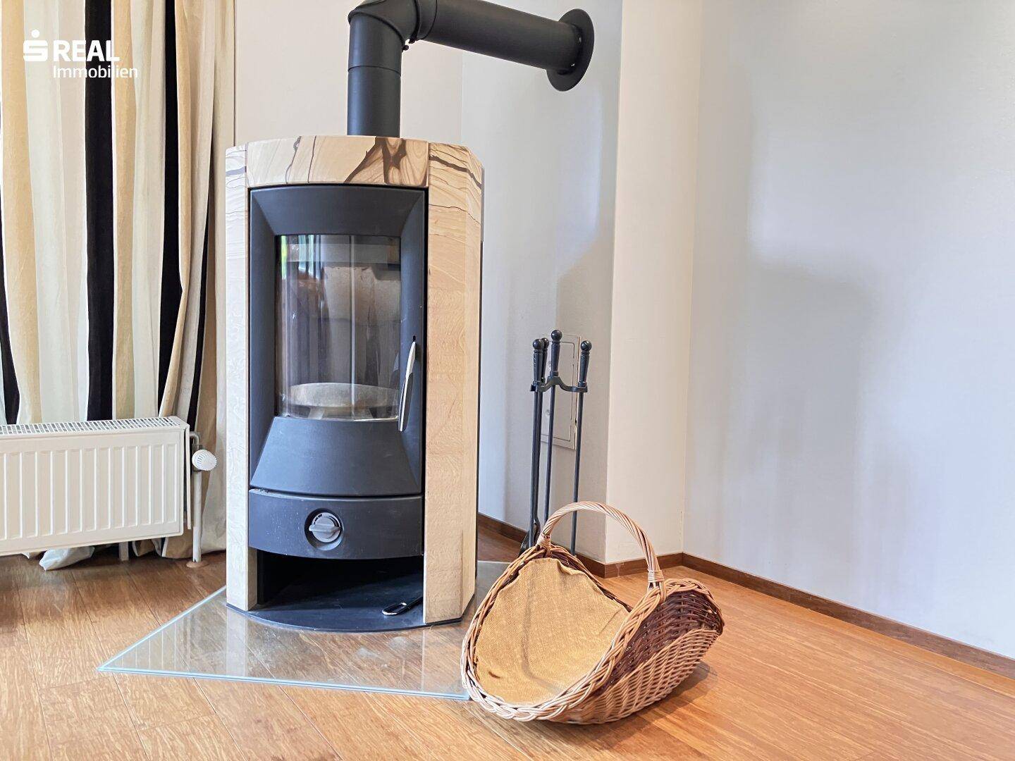 Moderner Kaminofen mit Holzverkleidung und Glasfront, daneben ein Korb für Brennholz.