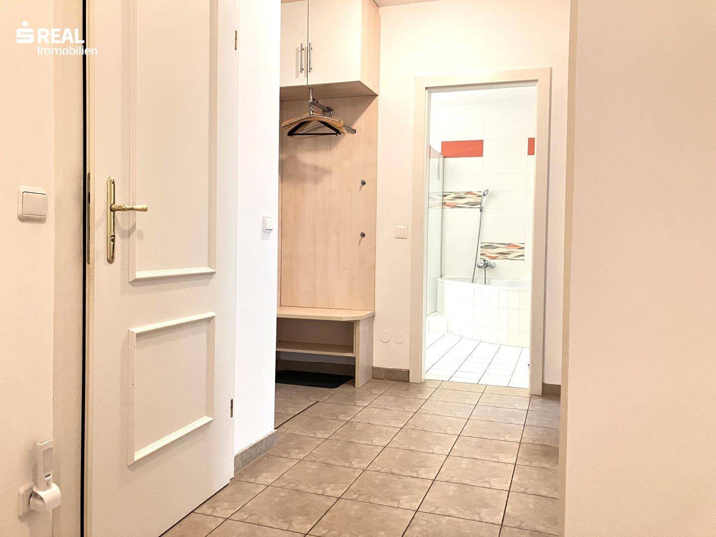 Flur mit Fliesenboden, integrierter Garderobe und Blick in das angrenzende Badezimmer.