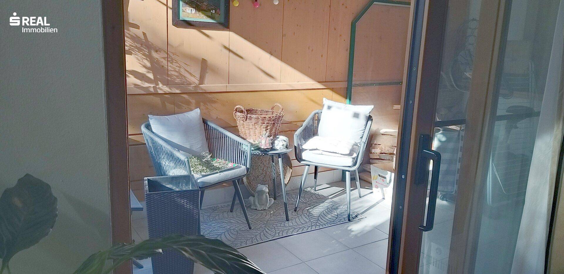 Blick von innen auf den möblierten Balkon mit bequemen Stühlen und viel Sonnenlicht.