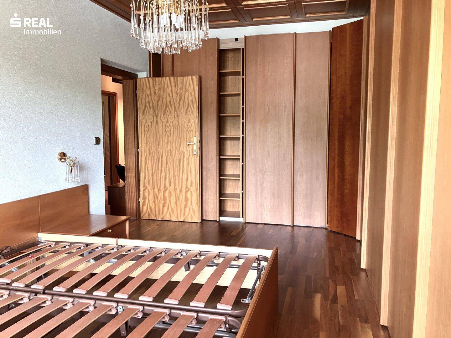Schlafzimmer mit Holzboden, Einbauschränken und einem Kronleuchter.