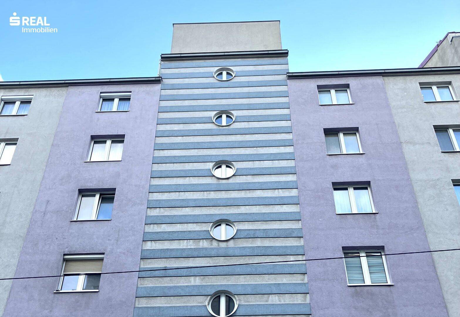Fassade eines Gebäudes mit markanten lila und blau-grauen Streifen sowie runden Fenstern.