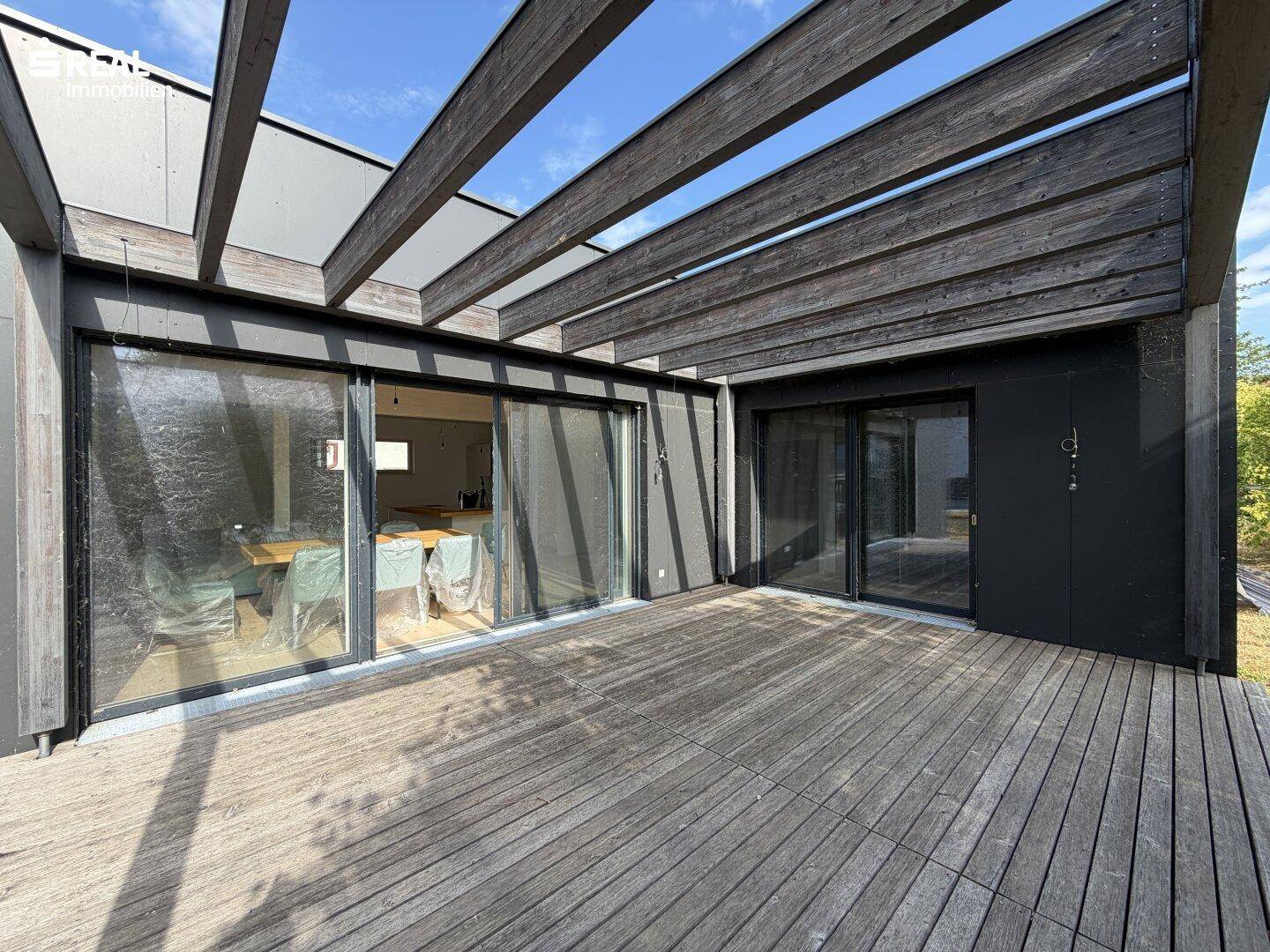 Geräumige Holzterrasse mit Pergola und großen Glasschiebetüren, die zum Innenbereich führen.