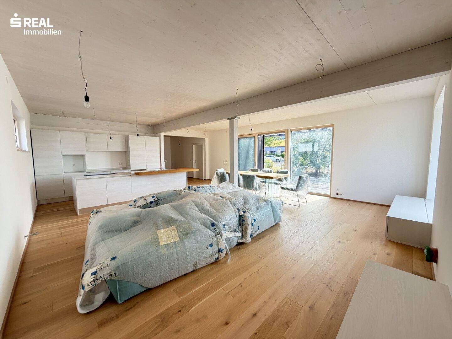 Offener Wohnbereich mit installierter Küche, Holzboden und verpackten Möbeln, bereit zum Einzug.