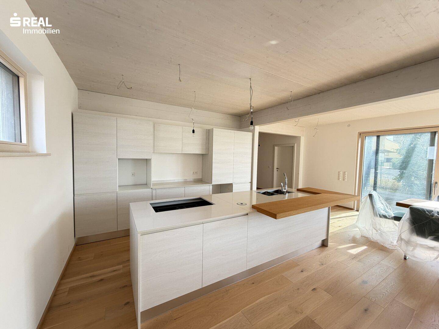 Moderne Einbauküche mit weißen Schränken, Kücheninsel und Holzarbeitsplatte in hellem Raum.