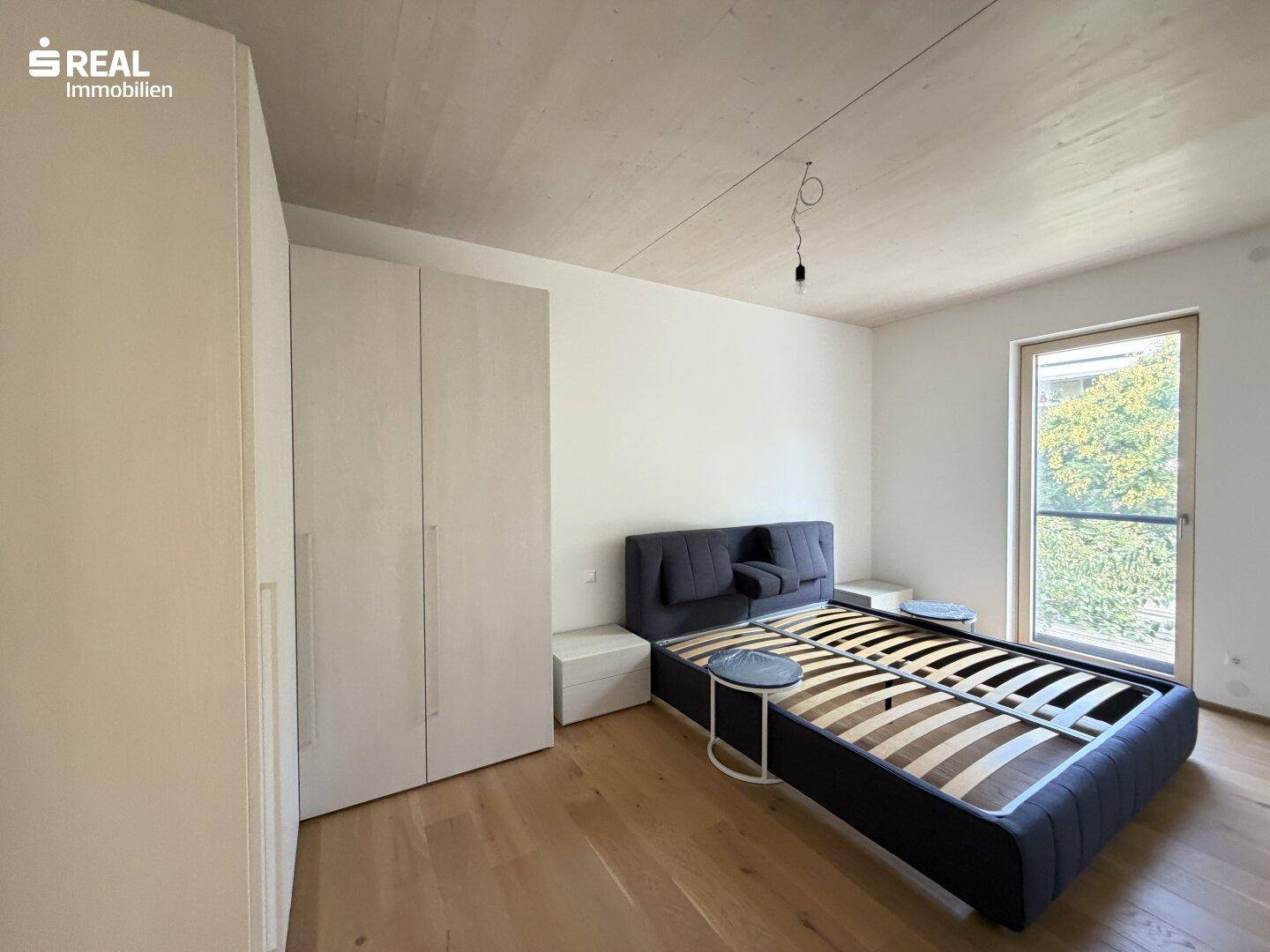 Helles Schlafzimmer mit Holzboden, großem Fenster und weißem Kleiderschrank, unmöbliert.