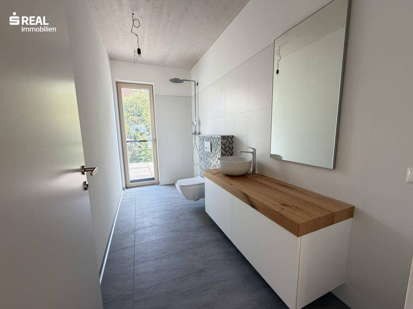 Modernes Badezimmer mit Holzarbeitsplatte, Aufsatzwaschbecken, Dusche und Fenster für Tageslicht.