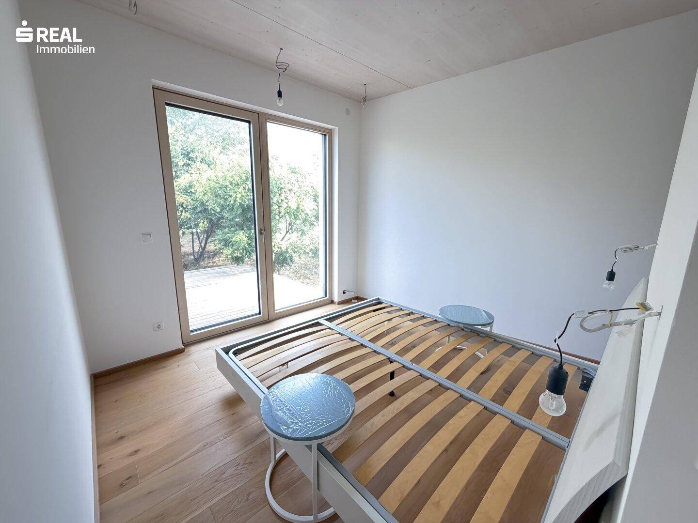 Helles Schlafzimmer mit Holzboden und großer Glastür, die Zugang zum Außenbereich bietet.