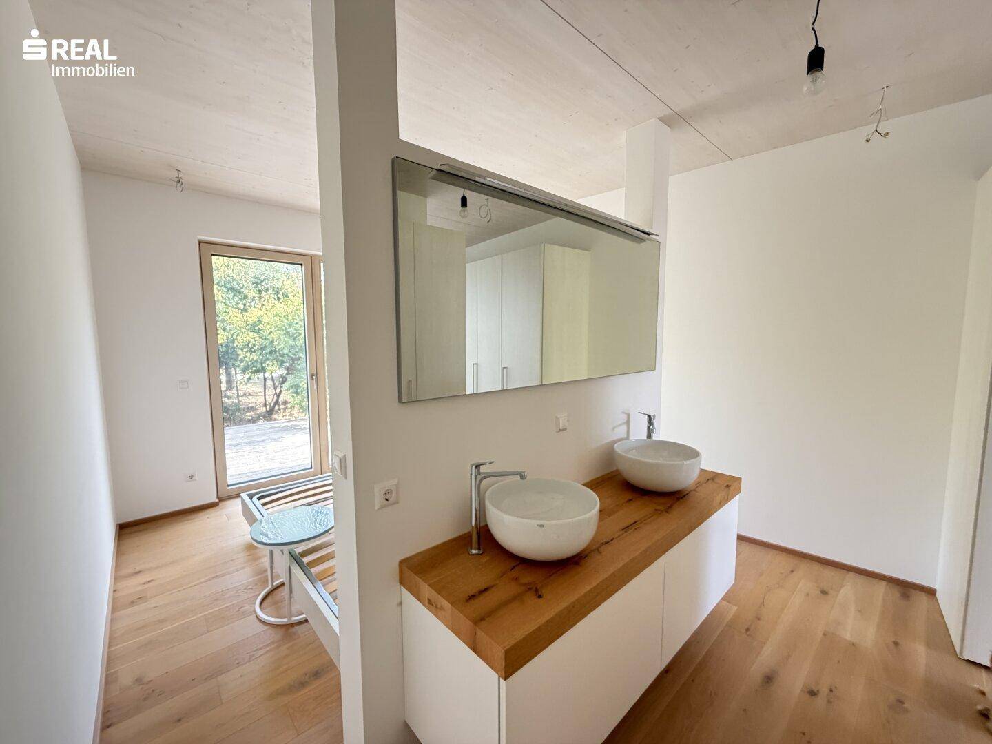 Modernes Badezimmer mit Doppelwaschbecken, großem Spiegel und Holzboden, hell und geräumig.