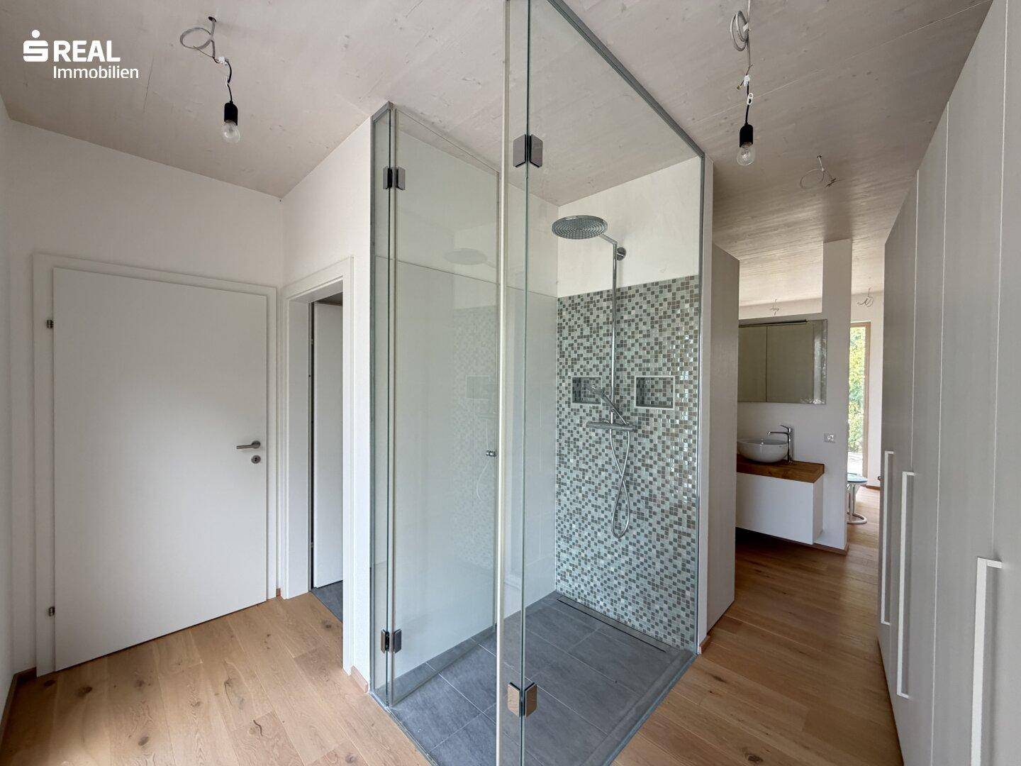 Modernes Badezimmer mit begehbarer Dusche, Glasabtrennung und Mosaikfliesen, sehr hell.