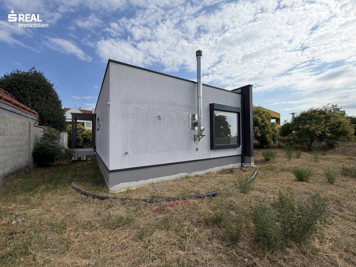 Seitenansicht des modernen Hauses mit Schornstein und Fenster, umgeben von trockenem Gras.