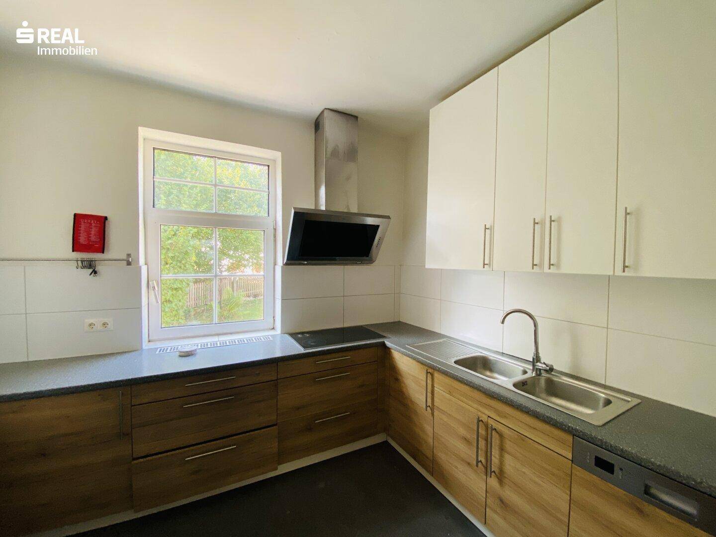 Moderne Küche mit Holzfronten, weißen Oberschränken und Dunstabzugshaube über dem Kochfeld.