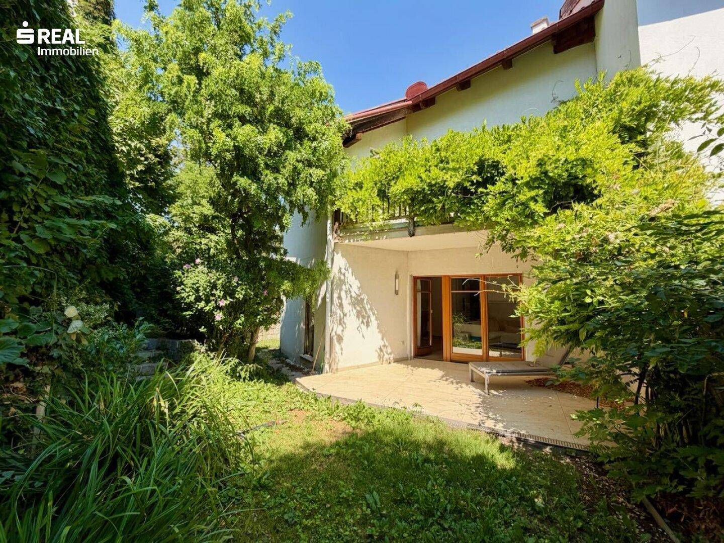 Gepflegter Gartenbereich mit Terrasse und üppiger Vegetation, ideal zum Entspannen im Freien.