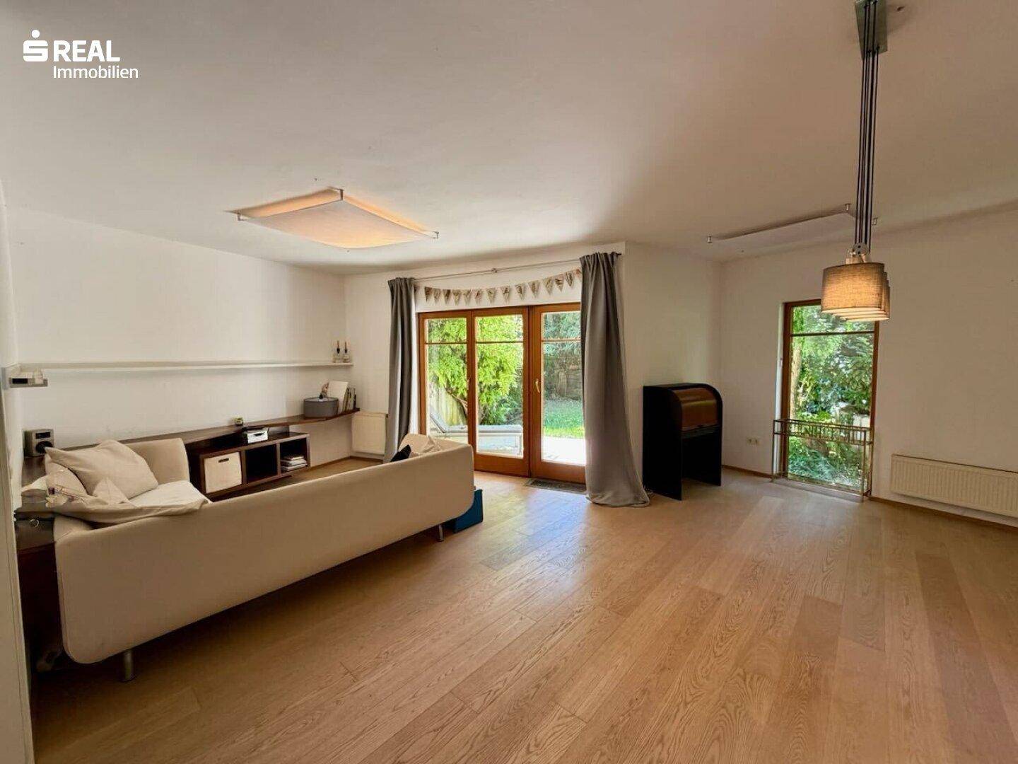 Geräumiges Wohnzimmer mit Holzboden, moderner Couch und direktem Zugang zum Garten.