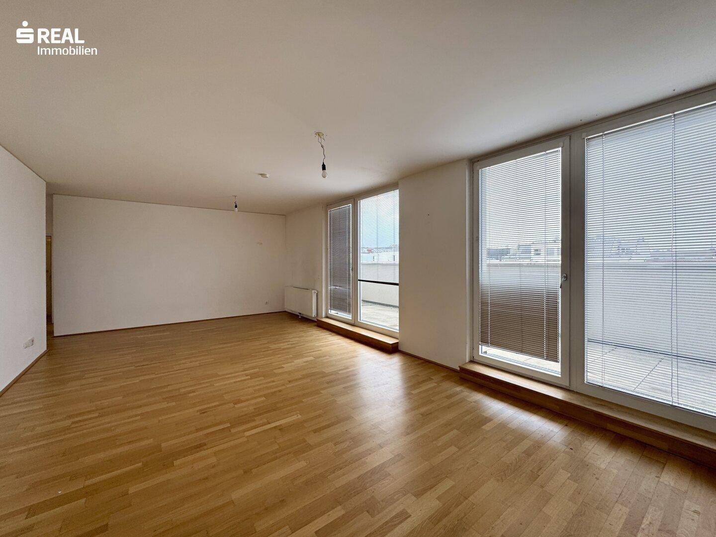 Geräumiges Wohnzimmer mit Holzboden und großen Fenstern, die Zugang zu einem Außenbereich bieten.