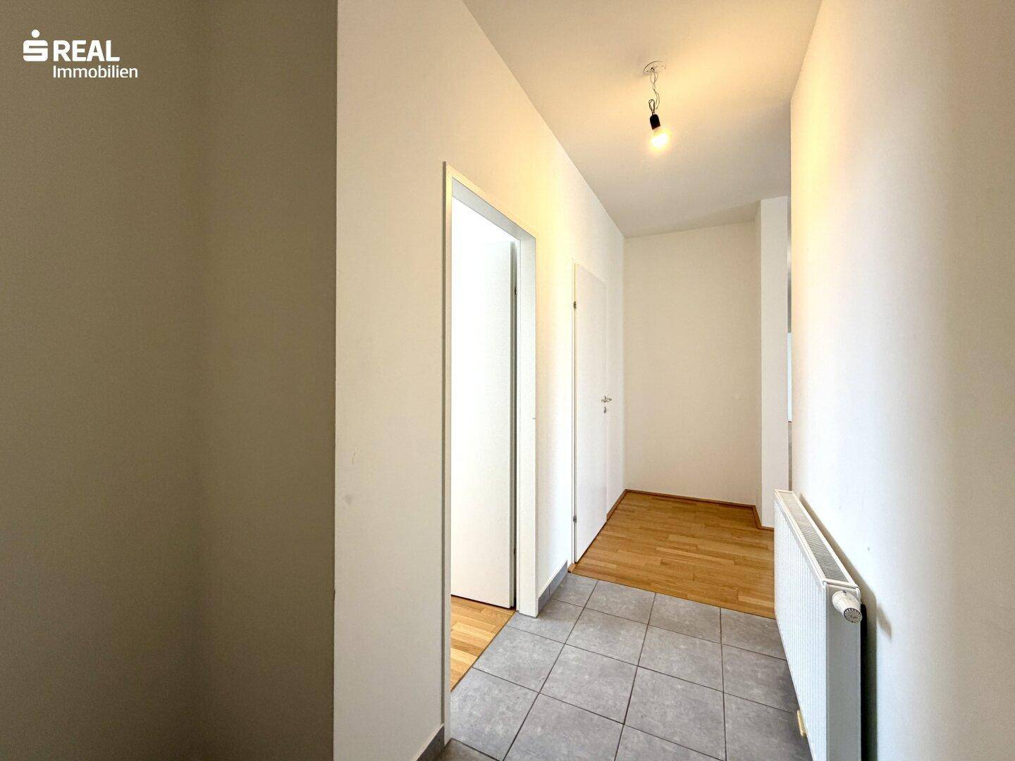 Heller Flur mit Fliesenboden, der in einen Bereich mit Holzboden übergeht.