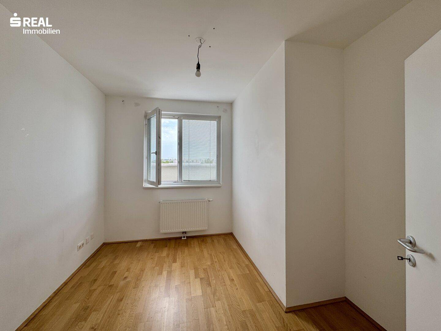 Helles Schlafzimmer mit Holzboden und einem Fenster, das viel Tageslicht hereinlässt.