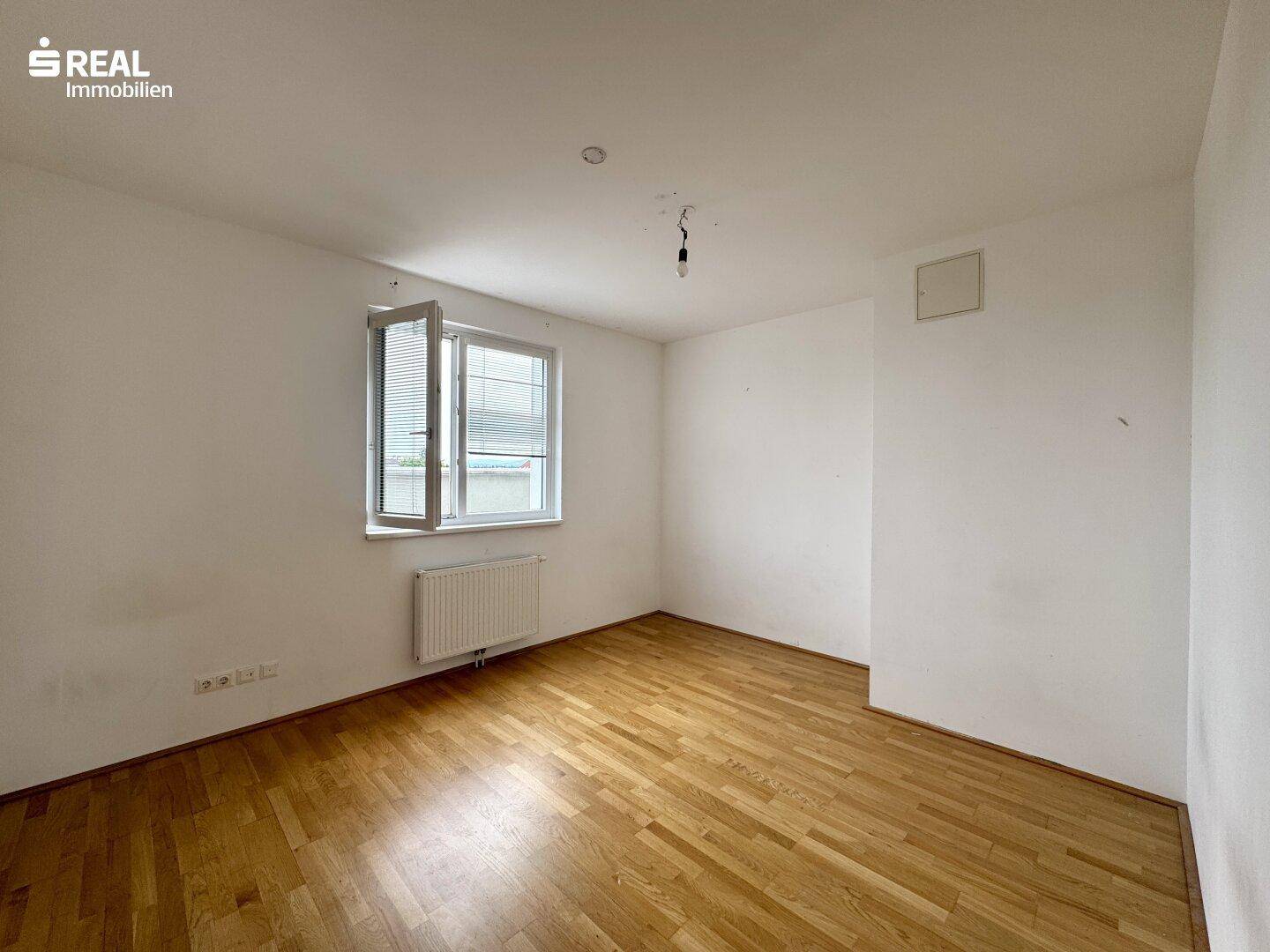 Leeres Zimmer mit Holzboden und Fenster, das auf eine Renovierung wartet.