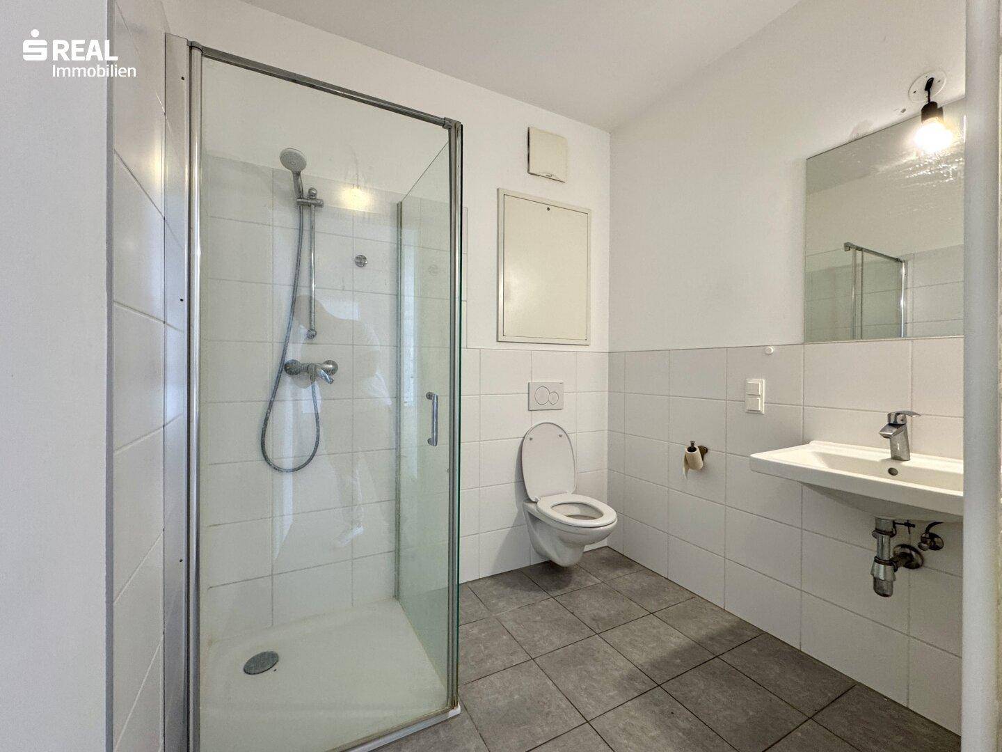 Badezimmer mit Duschkabine, WC, Waschbecken und weißen Wandfliesen.