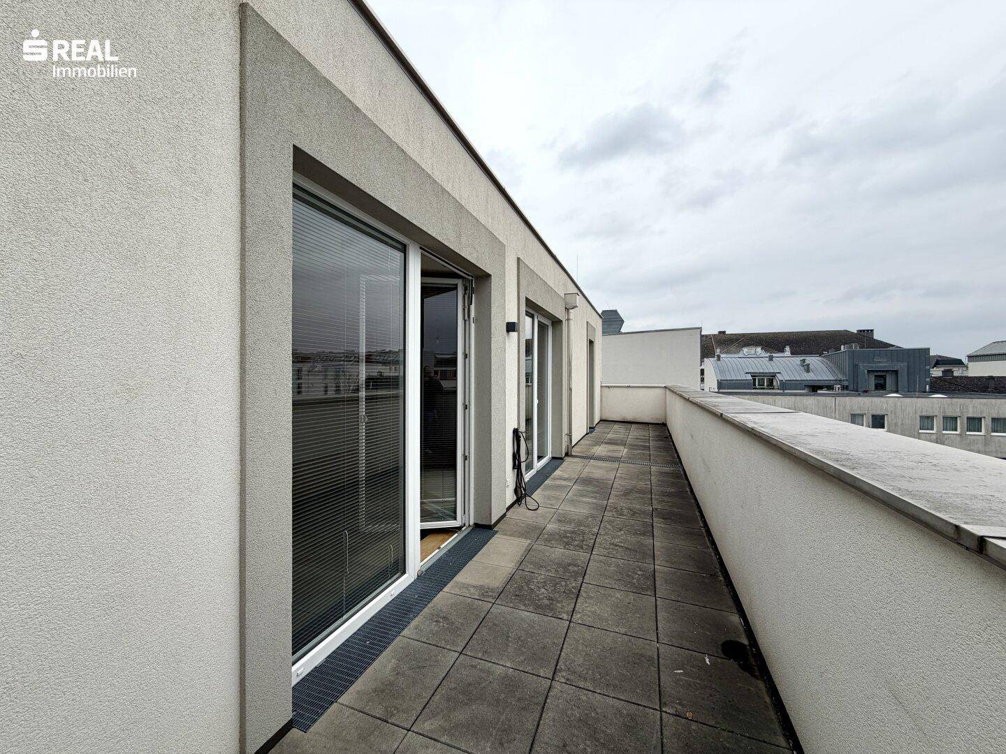 Geräumiger Balkon mit Fliesenboden und Zugang zu mehreren Zimmern.
