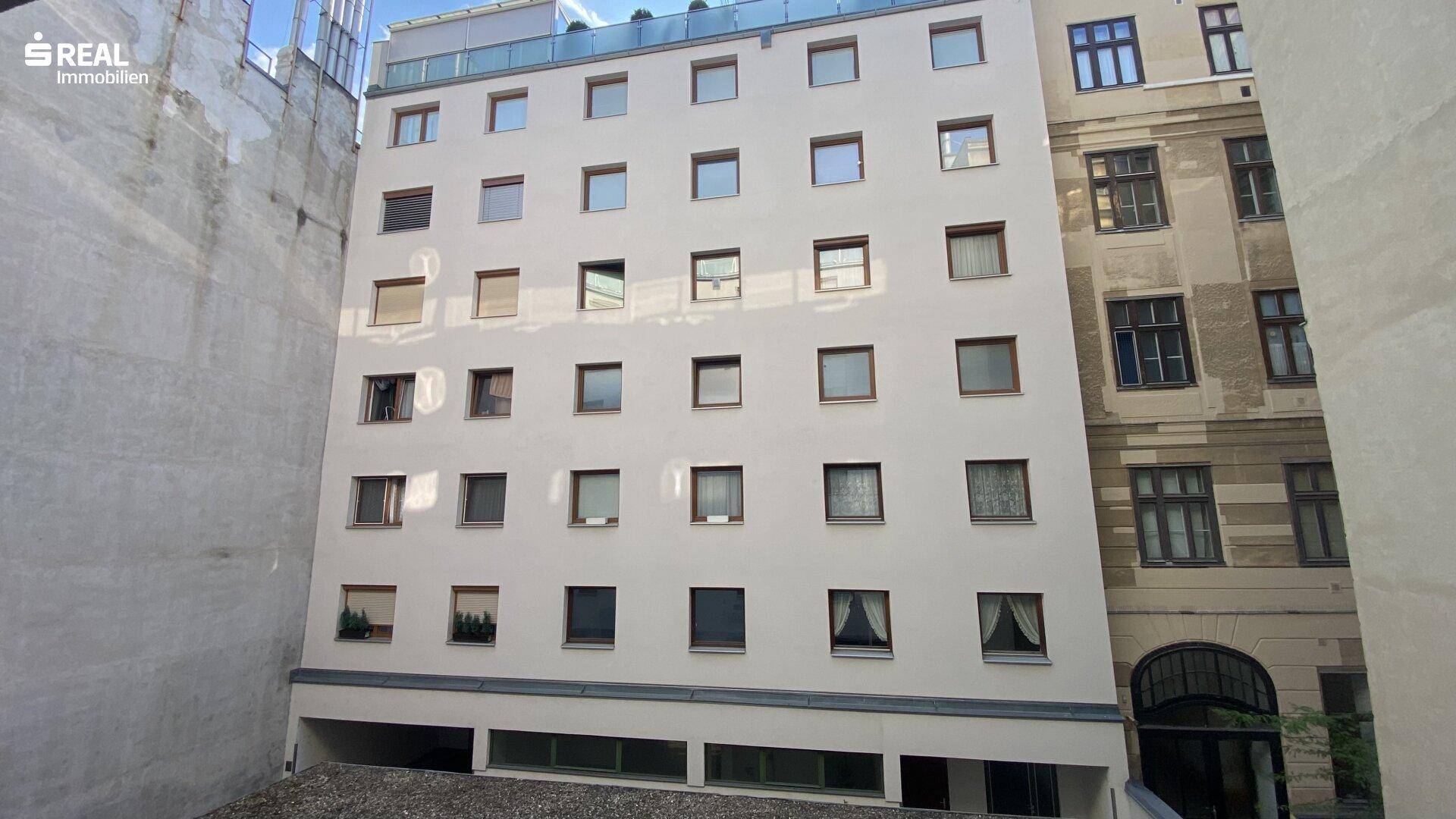 Moderne Gebäudefassade eines Mehrfamilienhauses mit vielen Fenstern, eingebettet zwischen anderen Gebäuden.