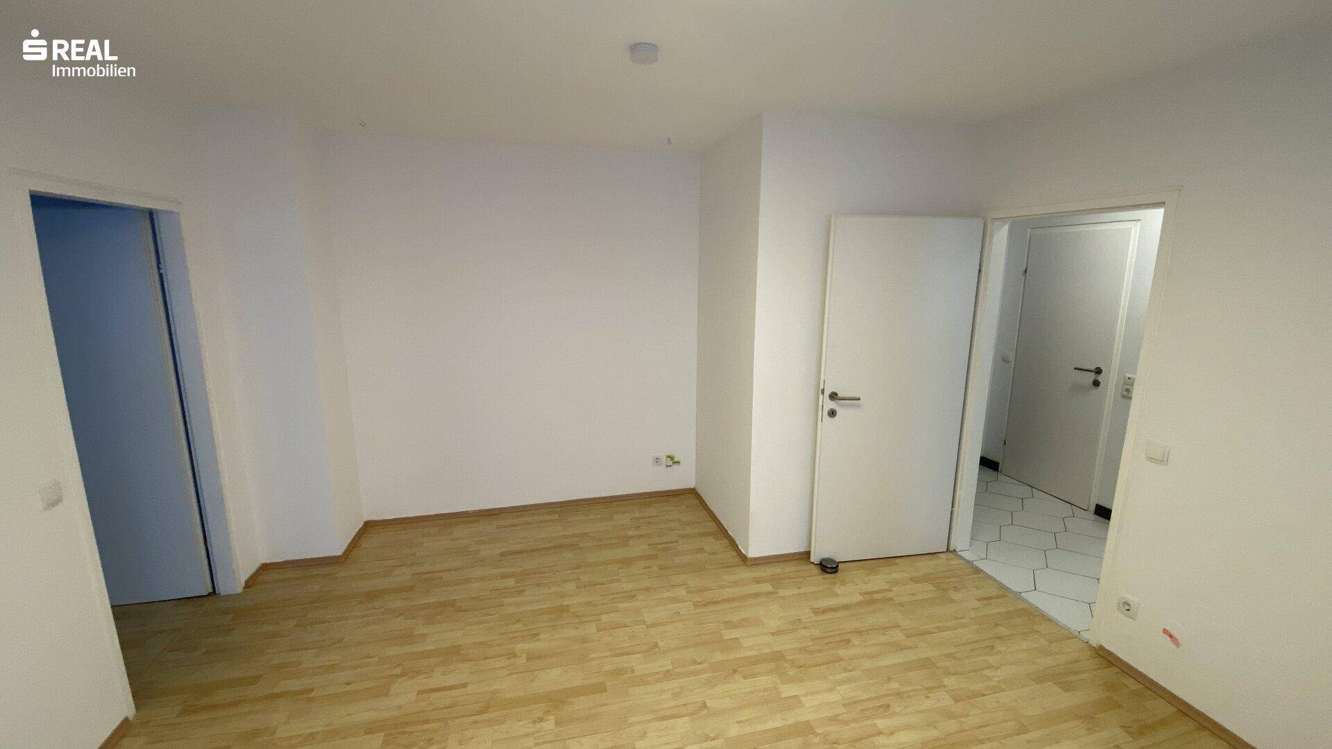 Geräumiges Zimmer mit hellem Parkettboden und zwei Türen, ideal für flexible Wohnkonzepte.