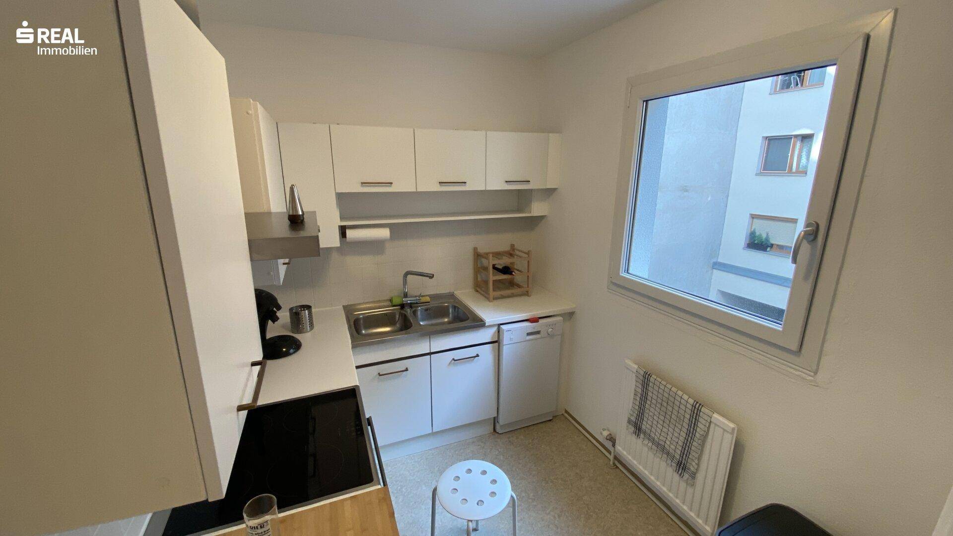 Funktionale Küche mit weißen Schränken, Spülbecken und Fenster, bietet ausreichend Arbeitsfläche.
