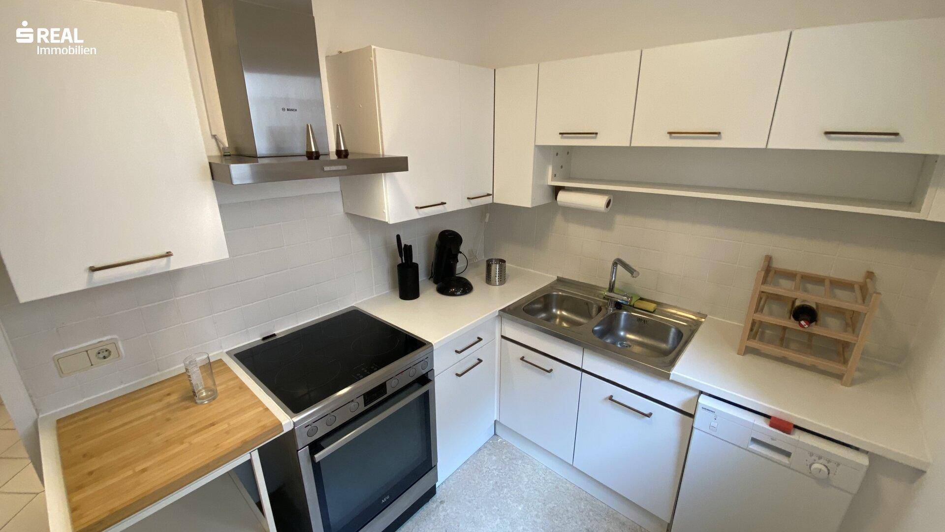 Moderne Einbauküche mit weißen Fronten, Herd, Backofen und Dunstabzugshaube für den täglichen Gebrauch.