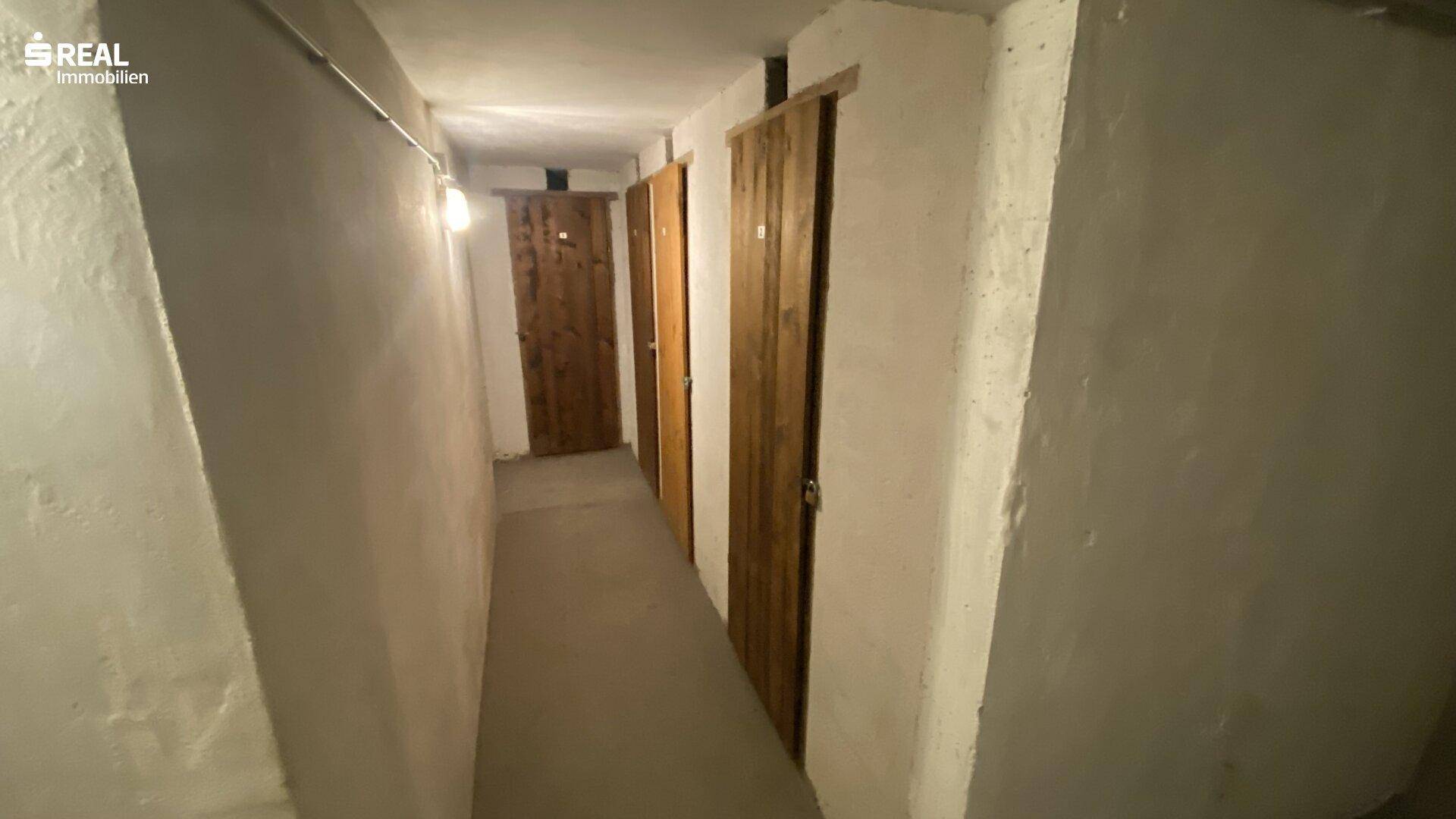 Kellergang mit mehreren Holzlagertüren, bietet individuelle Abstellmöglichkeiten für Bewohner.
