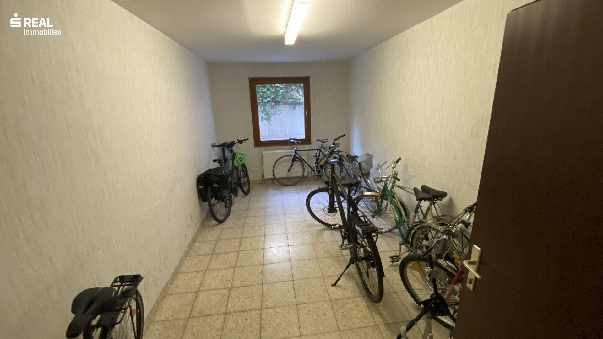 Geräumiger Fahrradraum im Untergeschoss mit mehreren Fahrrädern und einem Fenster für Belüftung.