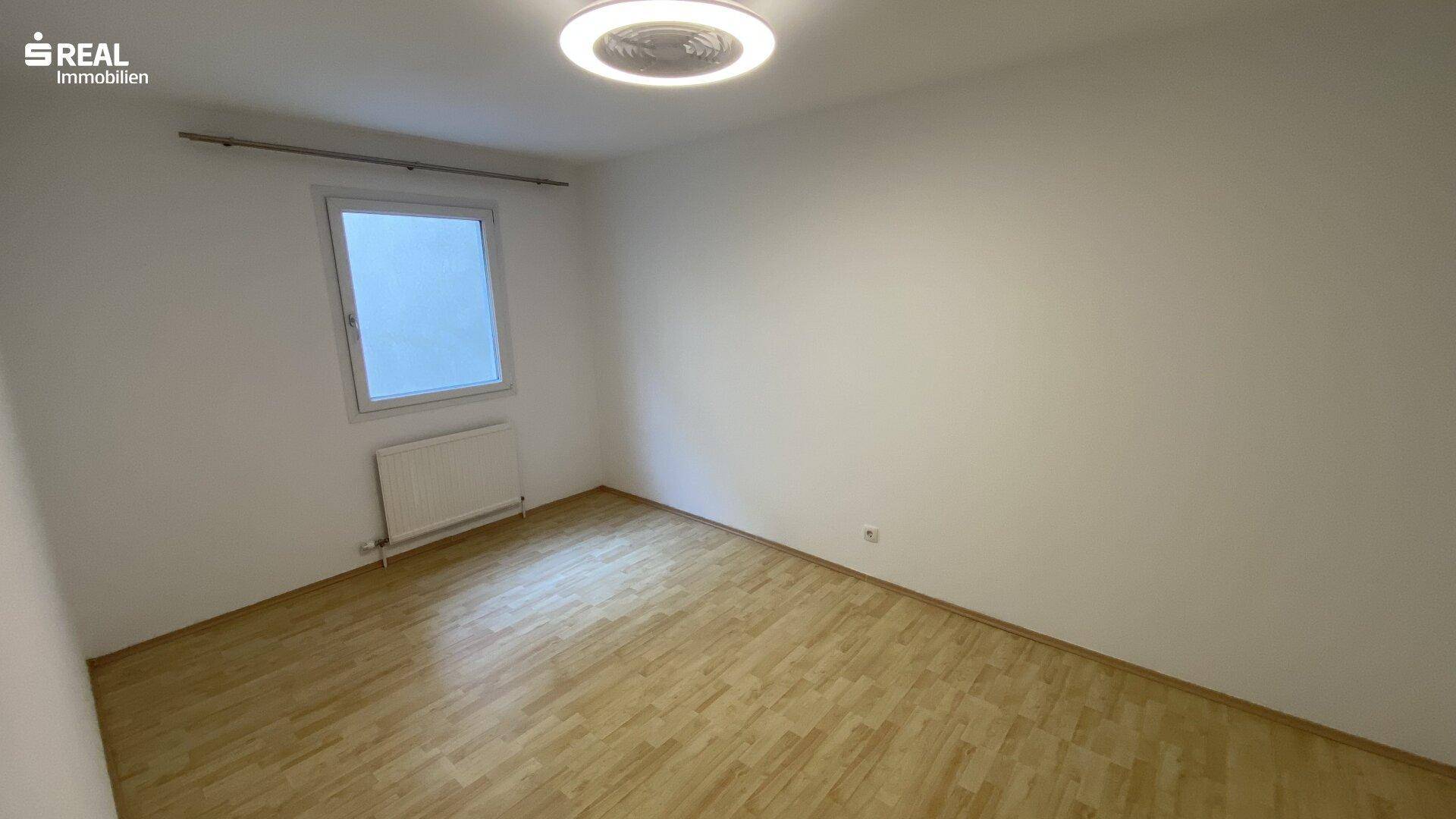 Freundliches Zimmer mit hellem Parkettboden und einem Fenster, das viel Tageslicht hereinlässt.