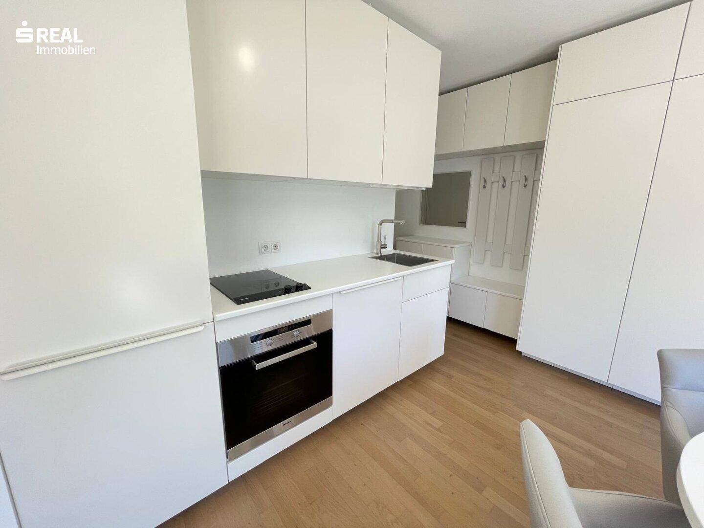 Moderne weiße Küchenzeile mit integrierten Geräten und hellem Holzfußboden.