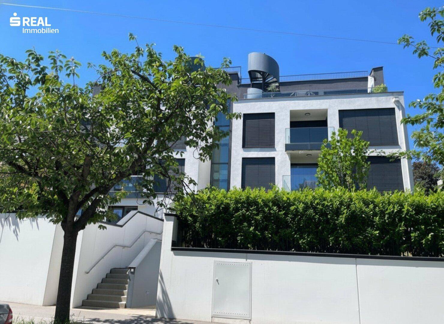 Modernes Wohngebäude mit weißer Fassade, großen Fenstern und einer Dachterrasse mit Wendeltreppe.
