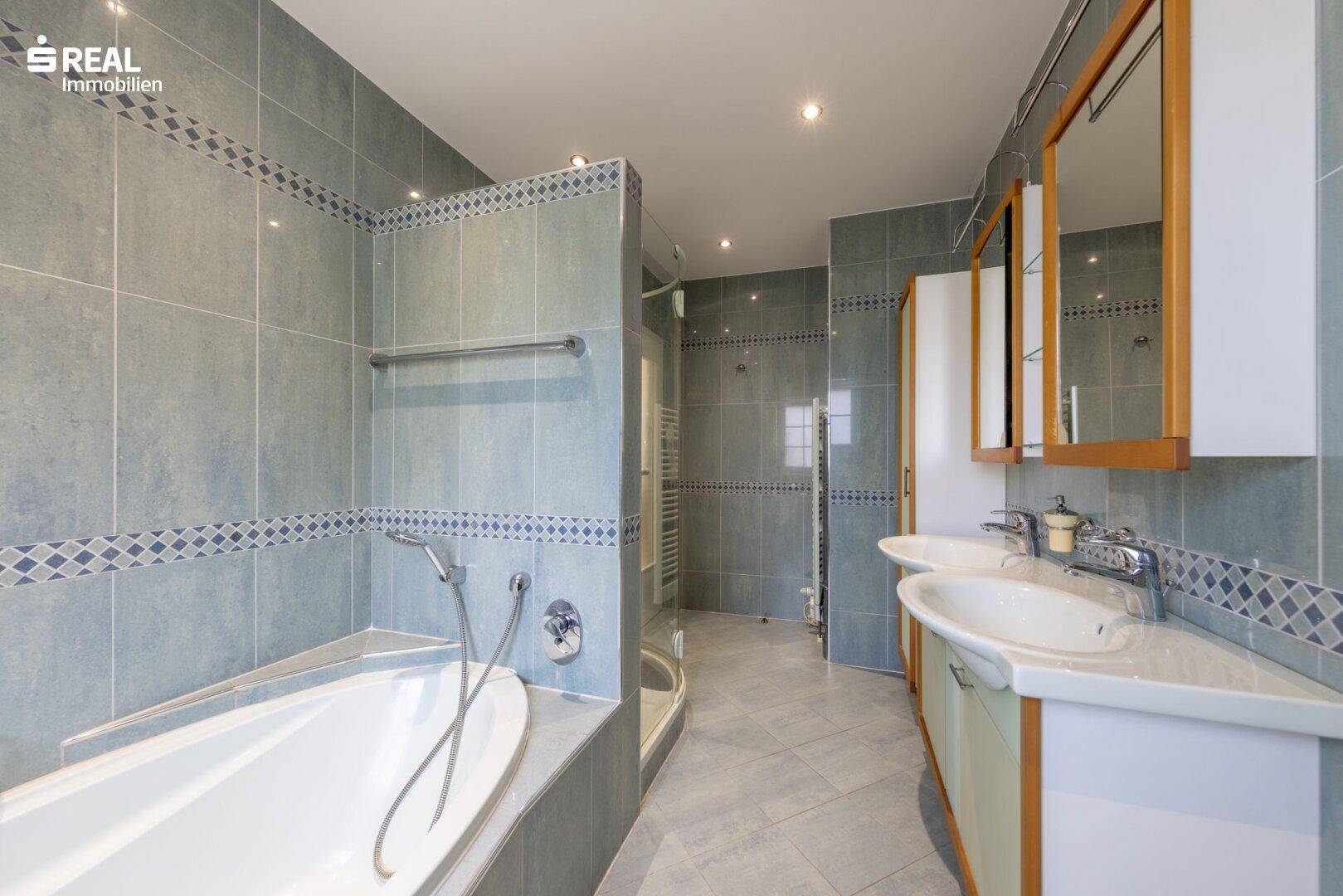 Geräumiges Badezimmer mit Doppelwaschbecken, Badewanne und Dusche, in blauen Fliesen gehalten.