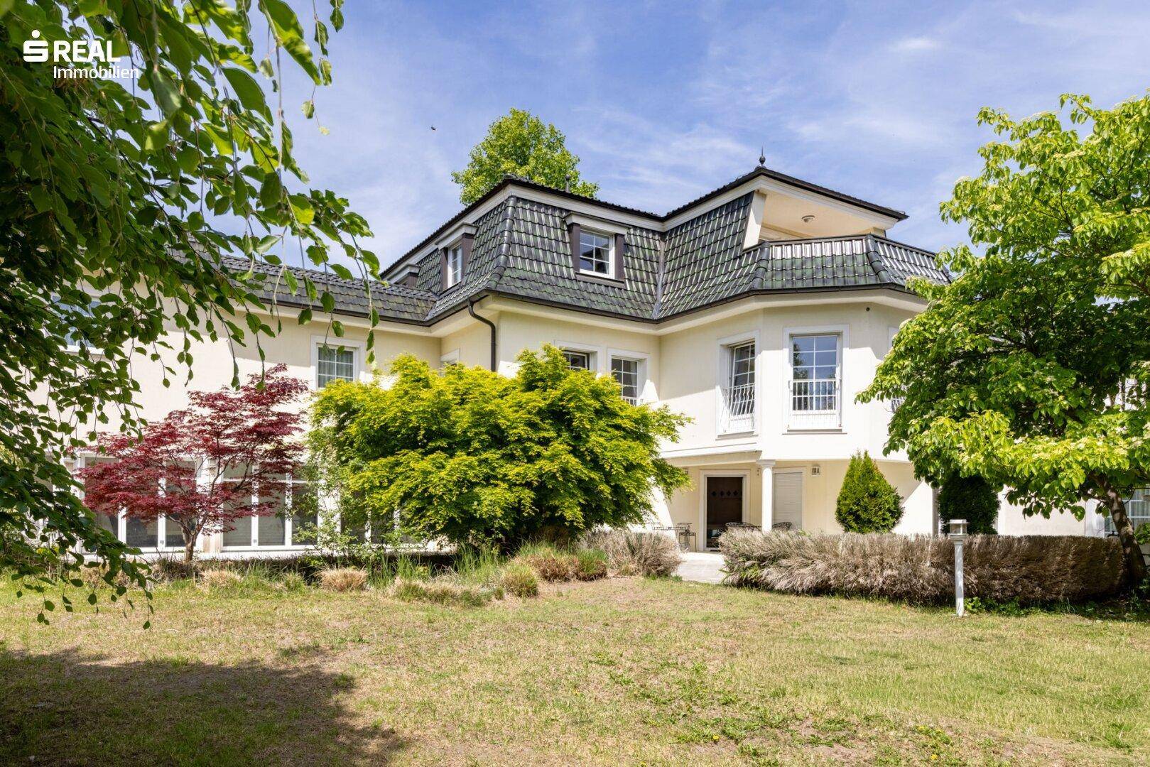 Gepflegter Vorgarten mit Rasenfläche und Bäumen, der die Villa umgibt.