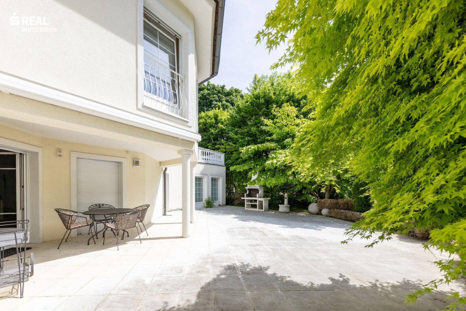 Sonniger Außenbereich mit Terrasse, Grillplatz und viel Grün, ideal für gesellige Abende.