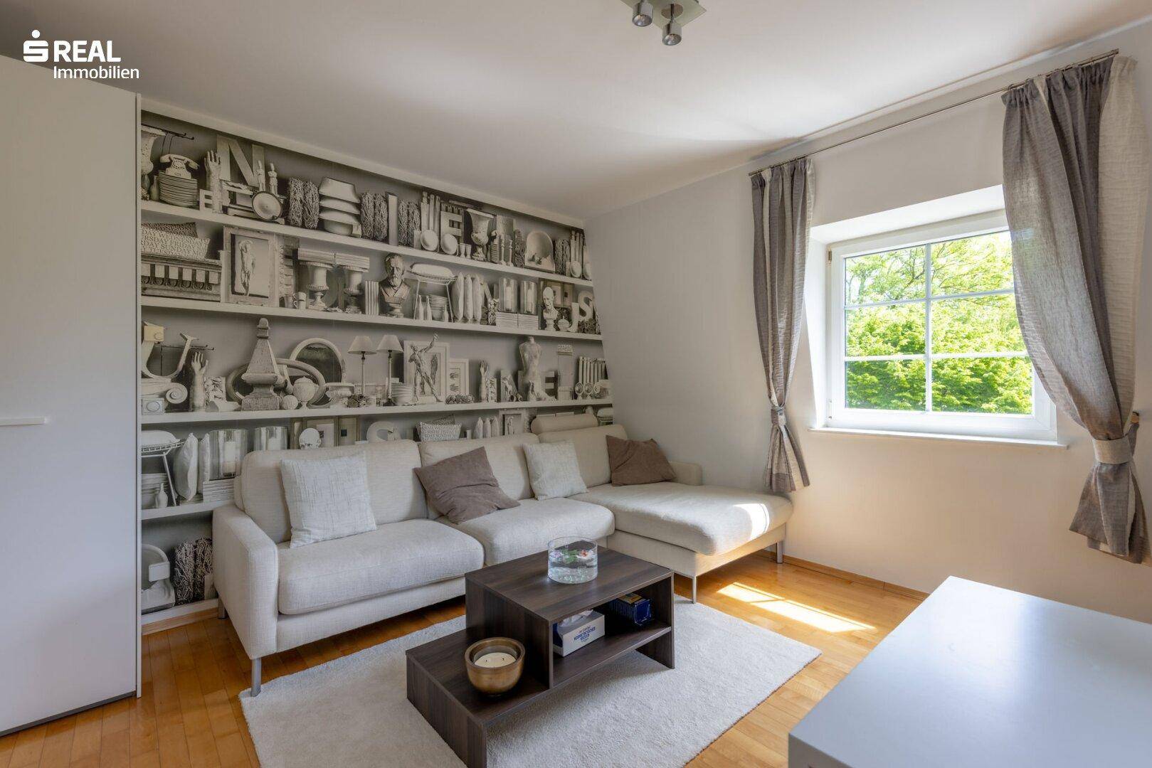 Gemütliches Wohnzimmer mit Sofa und einer auffälligen Bücherregal-Tapete, hell und modern.