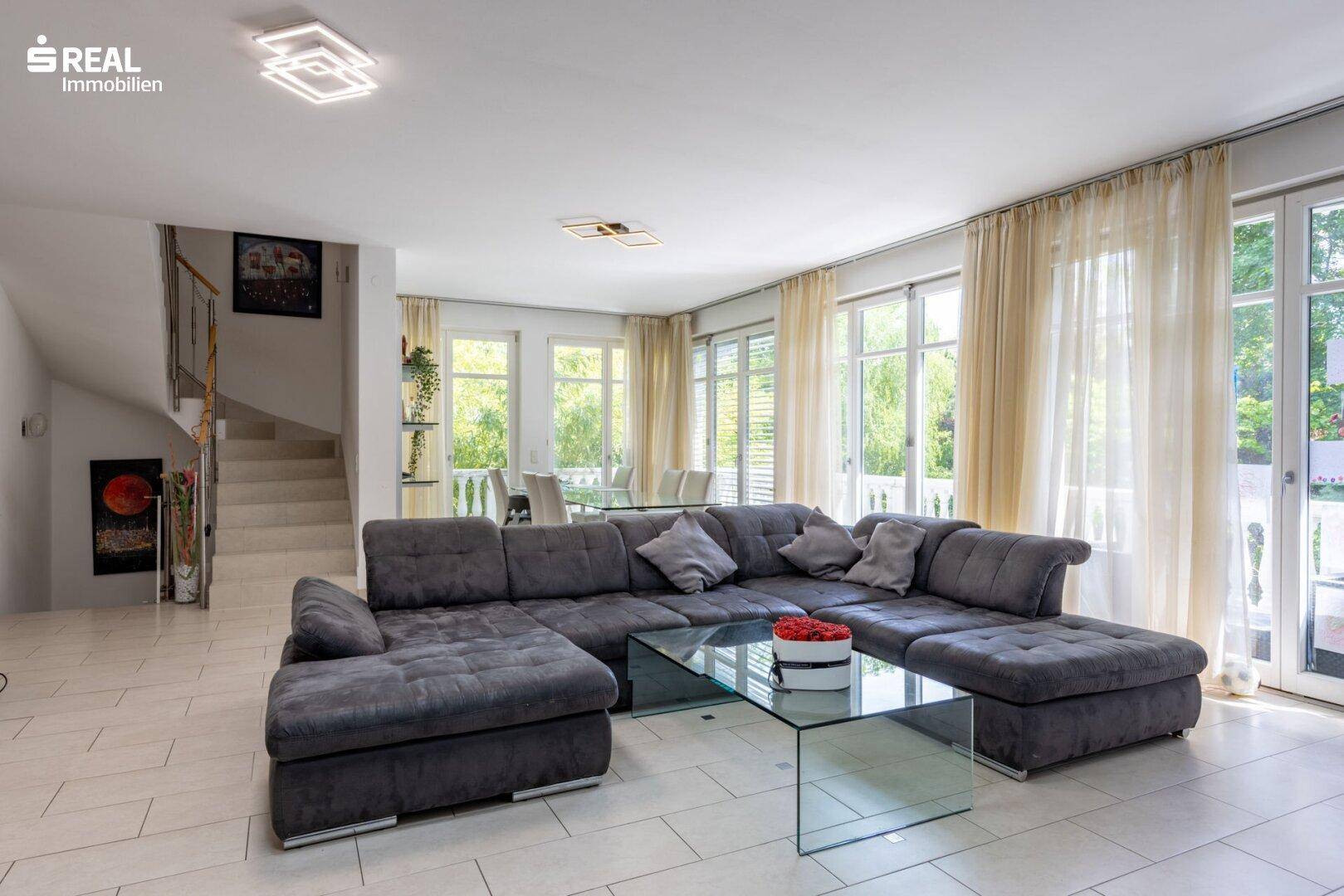 Gemütliches Wohnzimmer mit großer Eckcouch, Glastisch und Zugang zu Balkon und Treppe.