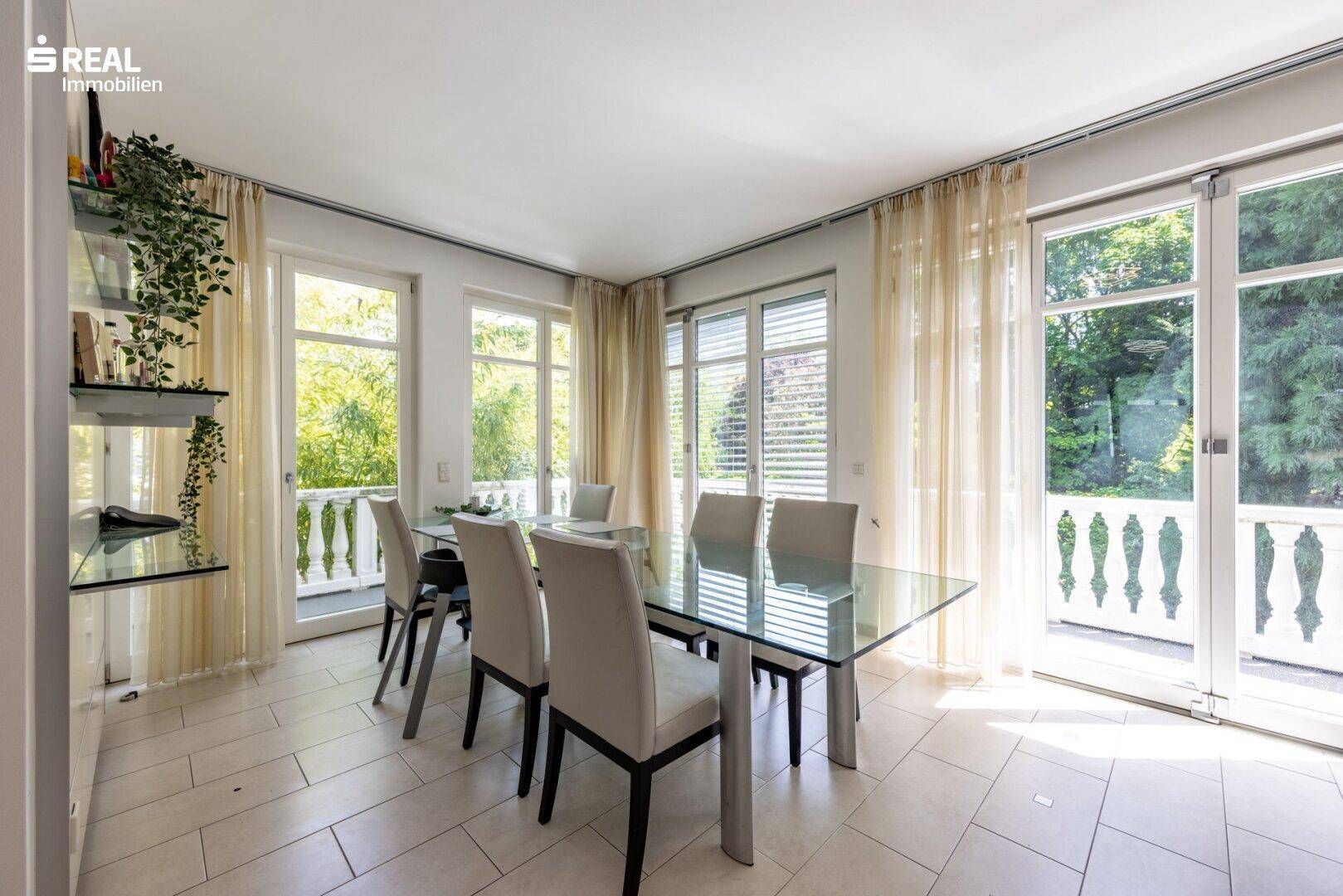 Heller Essbereich mit großem Glastisch, Fliesenboden und Zugang zu einem Balkon.
