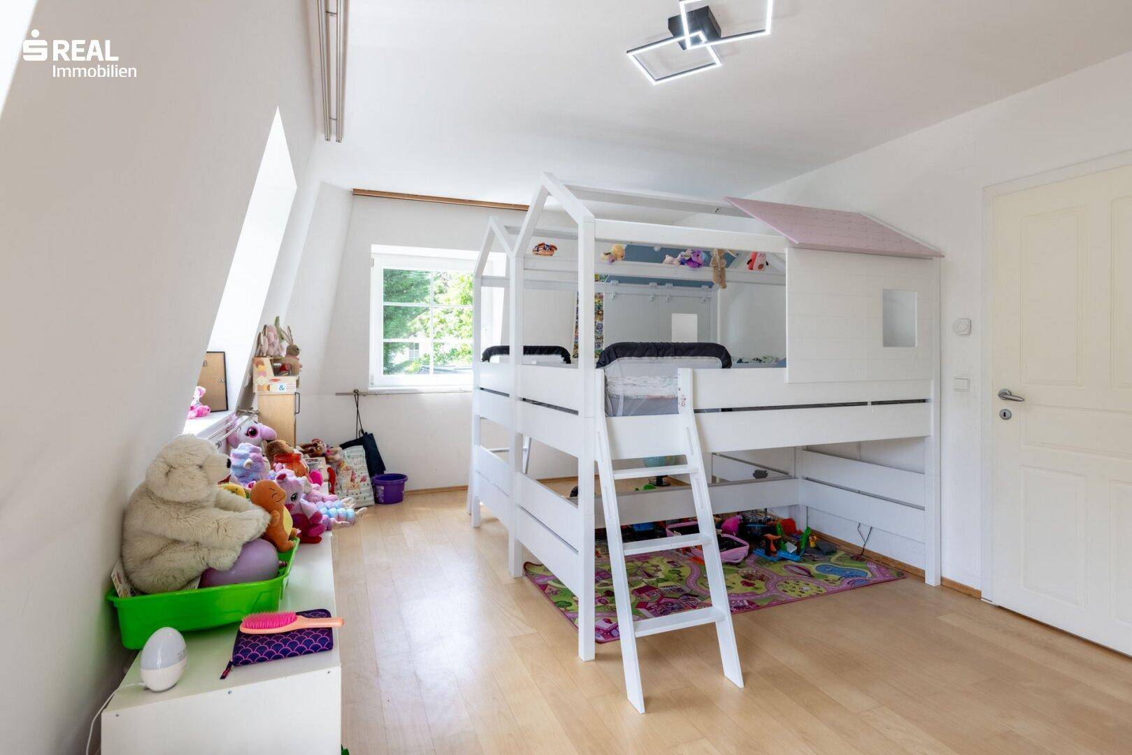 Freundliches Kinderzimmer mit Spielbereich, Hochbett und Holzboden.