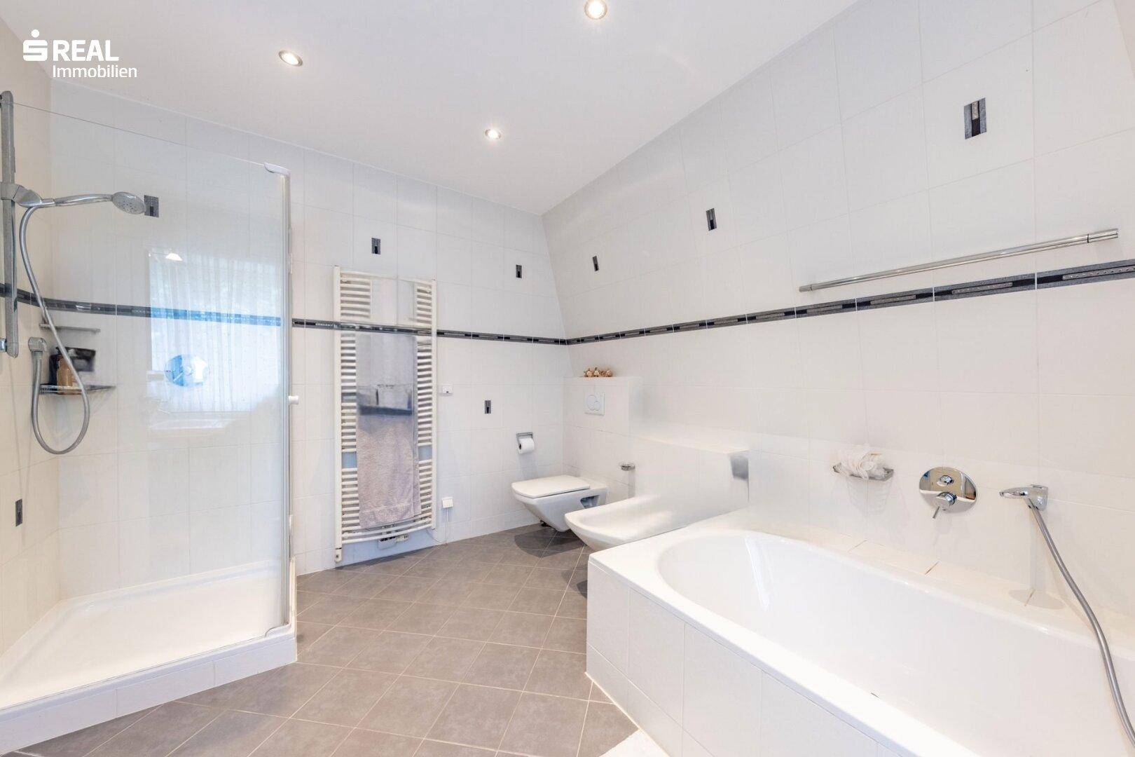 Modernes Badezimmer mit Dusche, Badewanne, WC und beheiztem Handtuchhalter.