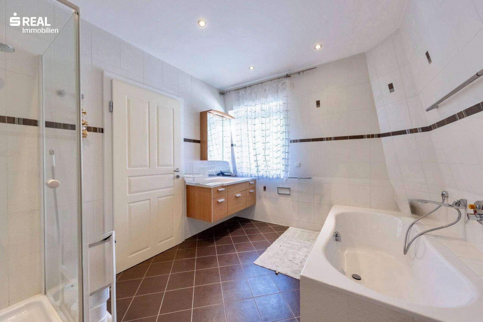 Badezimmer mit Badewanne, Dusche, Holzwaschtisch und Fenster.