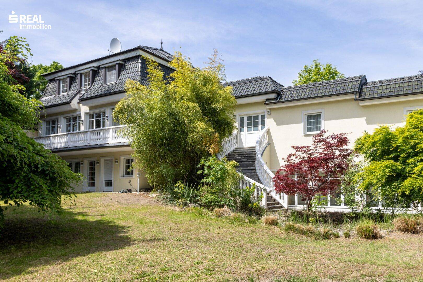 Gepflegter Gartenbereich mit Rasenfläche, Bäumen und Blick auf die Hausfassade.