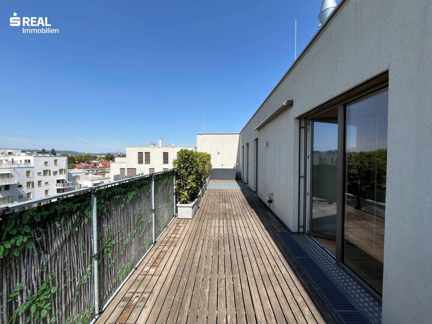 Lange Dachterrasse mit Holzboden und Bepflanzung, ideal für Entspannung im Freien.