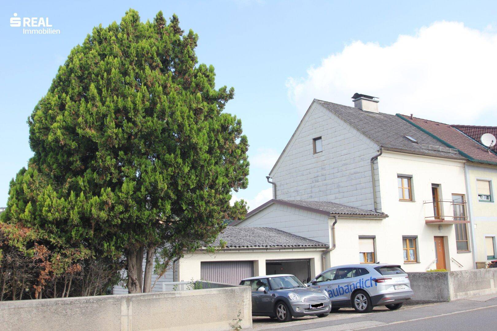 Seitenansicht des Hauses mit Garage und einem großen Baum im Vordergrund.