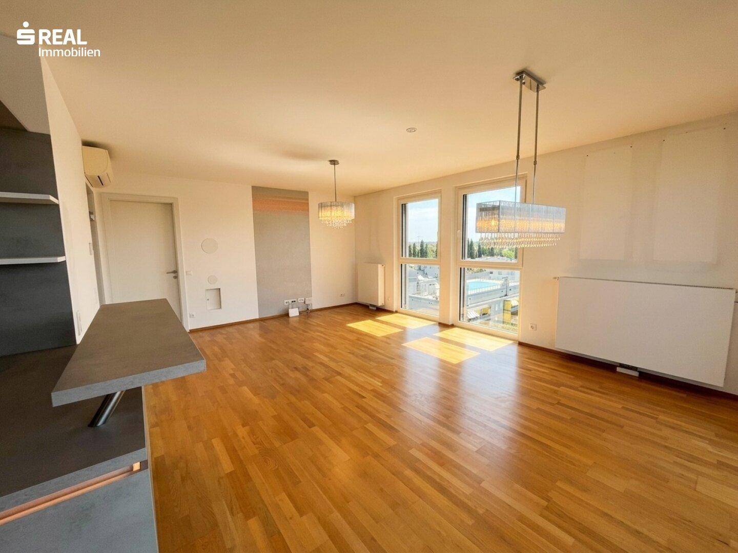 Geräumiger Wohnbereich mit Parkettboden, großen Fenstern und moderner Beleuchtung.